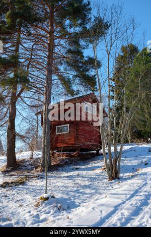 Eine malerische rote Hütte steht inmitten einer ruhigen Winterlandschaft in Västanvik, Dalarna. Stockfoto