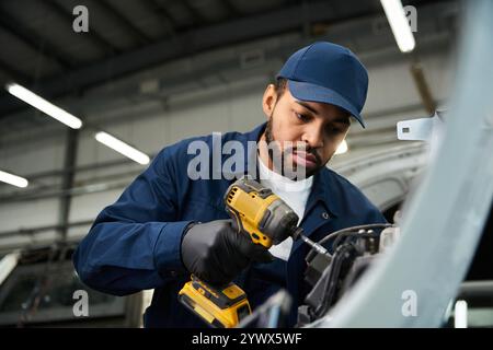 Ein gutaussehender Mechaniker konzentriert sich auf die Reparatur eines Motors mit seinem Elektrowerkzeug in der Werkstatt. Stockfoto