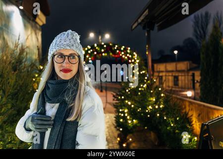 Glückliche junge Frau in gemütlicher Winterkleidung, die die Lichter der Feiertage bewundert Stockfoto