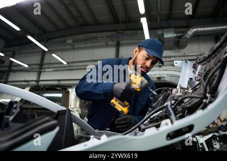 Der hübsche junge Mechaniker konzentriert sich auf die Reparatur von Fahrzeugkomponenten in einer modernen Garage. Stockfoto
