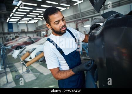 Ein erfahrener Mechaniker arbeitet fleißig an einem Auto in einer gut beleuchteten Autowerkstatt mit Fahrzeugen. Stockfoto