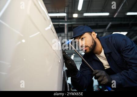 Ein junger Mechaniker inspiziert ein Fahrzeug in der Werkstatt sorgfältig unter Werkzeugen. Stockfoto