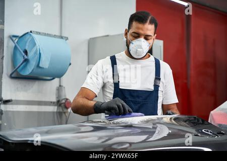 Erfahrener Mechaniker, der an einem Auto arbeitet, Schutzausrüstung trägt und konzentriert ist. Stockfoto