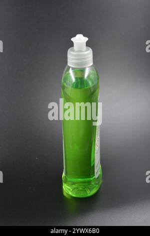 Klare, weiße, matte Flasche mit Spender, Geschirrreiniger. Eine mit einer hellgrünen, grünen Flüssigkeit gefüllte Kunststoffflasche befindet sich auf einem schwarzen Kunststoff. Stockfoto