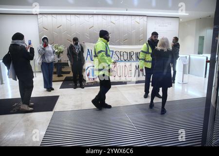 Bimingham, England, Großbritannien. Dezember 2024. Aktivisten protestieren im Empfangsbereich des Bürogebäudes mit einem Banner mit der Aufschrift „˜Allianz sichert Israels Völkermord-Maschine“ während der Demonstration. Pro-palästinensische Aktivisten zielen auf die Versicherungsbüros der Allianz in ihrem Colmore Building in Birmingham, die den Empfangsbereich besetzen und draußen protestieren. Sie zielen auf die Allianz ab, weil sie das israelische Rüstungsunternehmen Elbit Systems versichern und in das israelische Rüstungsunternehmen Elbit Systems investieren und entschlossen sind, den Druck des direkten Handelns aufrecht zu erhalten, damit es zu einem großen Nachteil wird, mit ihnen zusammenzuarbeiten. Sie verlangen, dass die Firma El abwirft Stockfoto