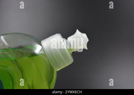 Klare, weiße, matte Flasche mit Spender, Geschirrreiniger. Eine mit einer hellgrünen, grünen Flüssigkeit gefüllte Kunststoffflasche befindet sich auf einem schwarzen Kunststoff. Stockfoto