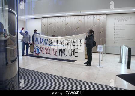 Bimingham, England, Großbritannien. Dezember 2024. Aktivisten protestieren im Empfangsbereich des Bürogebäudes mit einem Banner mit der Aufschrift „˜Allianz sichert Israels Völkermord-Maschine“ während der Demonstration. Pro-palästinensische Aktivisten zielen auf die Versicherungsbüros der Allianz in ihrem Colmore Building in Birmingham, die den Empfangsbereich besetzen und draußen protestieren. Sie zielen auf die Allianz ab, weil sie das israelische Rüstungsunternehmen Elbit Systems versichern und in das israelische Rüstungsunternehmen Elbit Systems investieren und entschlossen sind, den Druck des direkten Handelns aufrecht zu erhalten, damit es zu einem großen Nachteil wird, mit ihnen zusammenzuarbeiten. Sie verlangen, dass die Firma El abwirft Stockfoto