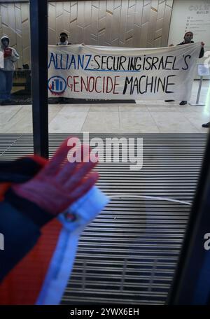 Bimingham, England, Großbritannien. Dezember 2024. Aktivisten protestieren im Empfangsbereich des Bürogebäudes, während Unterstützer während der Demonstration ihre rot bedeckten Hände auf das Glas drücken. Pro-palästinensische Aktivisten zielen auf die Versicherungsbüros der Allianz in ihrem Colmore Building in Birmingham, die den Empfangsbereich besetzen und draußen protestieren. Sie zielen auf die Allianz ab, weil sie das israelische Rüstungsunternehmen Elbit Systems versichern und in das israelische Rüstungsunternehmen Elbit Systems investieren und entschlossen sind, den Druck des direkten Handelns aufrecht zu erhalten, damit es zu einem großen Nachteil wird, mit ihnen zusammenzuarbeiten. Sie verlangen, dass die Firma Elbit Systems abwirft. Stockfoto