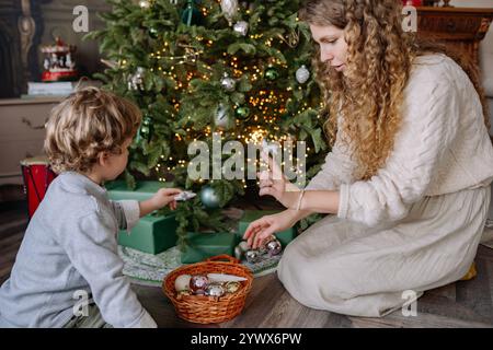 Feiern Sie Weihnachten und Neujahr mit der Familie, während Mutter und Sohn den Baum gemeinsam in einem gemütlichen Wohnzimmer schmücken Stockfoto