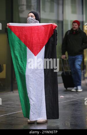 Bimingham, England, Großbritannien. Dezember 2024. Ein Aktivist mit palästinensischer Flagge protestiert draußen, während Arbeiter während der Demonstration um den Rücken des Gebäudes geschickt werden. Pro-palästinensische Aktivisten zielen auf die Versicherungsbüros der Allianz in ihrem Colmore Building in Birmingham, die den Empfangsbereich besetzen und draußen protestieren. Sie zielen auf die Allianz ab, weil sie die israelische Rüstungsfirma Elbit Systems versichern und in diese investieren. Sie verlangen, dass die Firma Elbit Systems abwirft. (Kreditbild: © Martin Pope/ZUMA Press Wire) NUR REDAKTIONELLE VERWENDUNG! Nicht für kommerzielle ZWECKE! Stockfoto