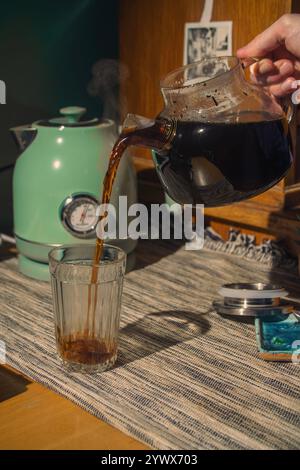 Gießen Sie eine Tasse frisch gebrühten aromatischen Kaffees in ein klares, elegantes Glasgefäß Stockfoto