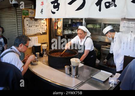 Frau, die Rindereintopf in einem Verkaufsstand am Straßenrand serviert, in Tsukiji, Chuo City, Tokio, Japan, Asien. Stockfoto