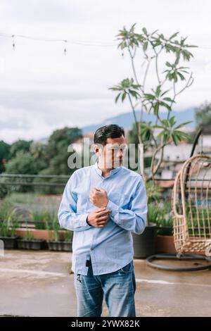 Ein südostasiatischer Mann, der sein Hemdärmel anpasst, in einem lässigen Moment festgehalten und für Sauberkeit, Vorbereitung oder Alltagsroutine steht Stockfoto
