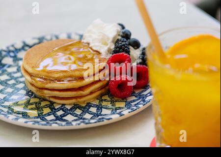 Ein köstlicher Stapel goldbrauner Pfannkuchen mit Honig, gekrönt mit einem Klecks Schlagsahne und mit frischen Himbeeren und Blackberri geschmückt Stockfoto