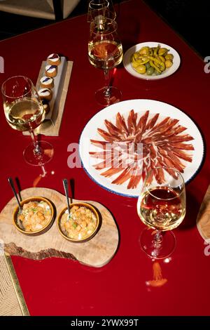 Ein lebendiger Esstisch mit einer Auswahl an Gourmetgerichten. In der Mitte befindet sich ein schön angelegter Teller mit geräuchertem Schinken, der von eleganten Gläsern umgeben ist Stockfoto