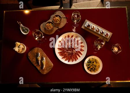 Ein lebendiger Esstisch mit einer Auswahl an Gourmetgerichten. In der Mitte befindet sich ein schön angelegter Teller mit geräuchertem Schinken, der von eleganten Gläsern umgeben ist Stockfoto