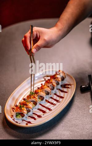 Nahaufnahme einer Hand mit einer Goldzange, um ein Stück Sushi sanft zu heben. Stockfoto