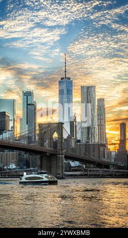 Das Foto zeigt die Brooklyn Bridge bei Sonnenuntergang von Brooklyn, wobei Wolken auf dem Wasser reflektieren. Die Skyline, ein moderner Wolkenkratzer im Hinterland Stockfoto