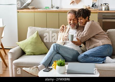 Ein fröhliches Paar teilt sich einen zärtlichen Moment, während er in seinem einladenden Zuhause Kaffee schlürft. Stockfoto