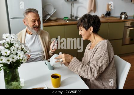 Ein fröhliches, reifes Paar teilt sich einen Moment des Lachens, während er gemeinsam Kaffee genießt. Stockfoto