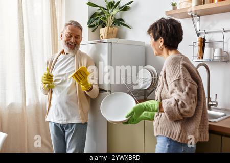 Ein fröhliches, reifes Paar wäscht gerne Geschirr und lacht in der warmen Küche Stockfoto