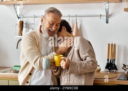 Ein reifes Paar umarmt sich herzlich, während es seinen Kaffee in einer fröhlichen Küchenatmosphäre genießt. Stockfoto