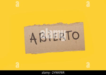 Abierto handgeschrieben auf einem Stück Pappe auf gelbem Hintergrund mit Kopierraum (trad. Offen) Stockfoto