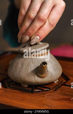 Legen Sie den Deckel vorsichtig von Hand auf eine traditionelle Teekanne während einer ruhigen Teezeremonie Stockfoto