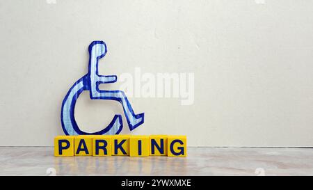 Rollstuhlsymbol für Behinderte aus farbigem Karton mit PARKPLATZ auf Holzwürfeln auf grauem Hintergrund Kopierraum. Stockfoto