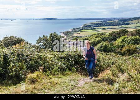 Eine weibliche Walkerin, die Treppen auf dem South West Coast Path mit Blick auf Ringstead, Portland Bill im Hintergrund, Dorset, Großbritannien, klettert Stockfoto