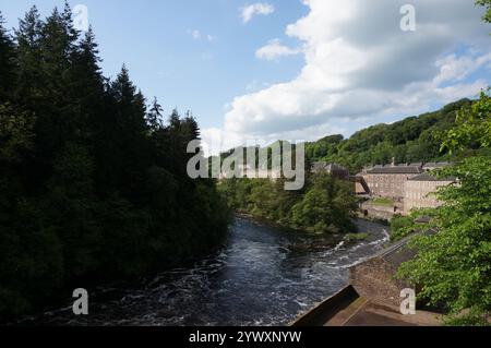 Blick auf einen Fluss, Bäume und alte Gebäude, New Lanark Welterbestätte in der Nähe des Flusses Clyde, New Lanark, Schottland Stockfoto