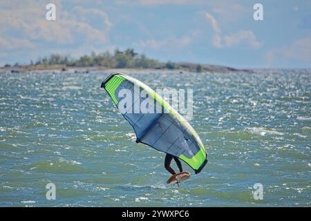 Der Mann ist Flügelfolierung mit handgehaltenem aufblasbarem Flügel und Tragflächensurfbrett im Meer im Sommer. Fahrer auf einem Windflügel-Board, surft in den Wellen. Stockfoto