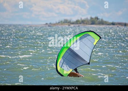 Der Mann ist Flügelfolierung mit handgehaltenem aufblasbarem Flügel und Tragflächensurfbrett im Meer im Sommer. Fahrer auf einem Windflügel-Board, surft in den Wellen. Stockfoto