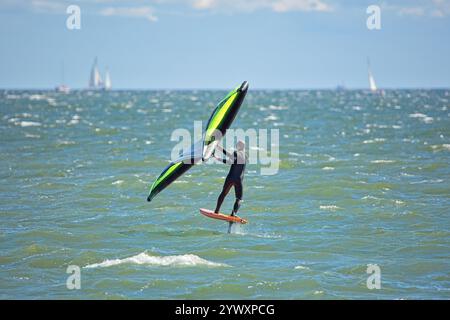 Der Mann ist Flügelfolierung mit handgehaltenem aufblasbarem Flügel und Tragflächensurfbrett im Meer im Sommer. Fahrer auf einem Windflügel-Board, surft in den Wellen. Stockfoto