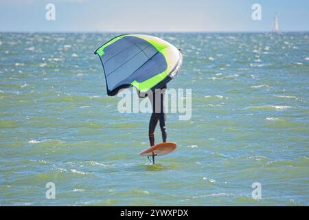 Der Mann ist Flügelfolierung mit handgehaltenem aufblasbarem Flügel und Tragflächensurfbrett im Meer im Sommer. Fahrer auf einem Windflügel-Board, surft in den Wellen. Stockfoto