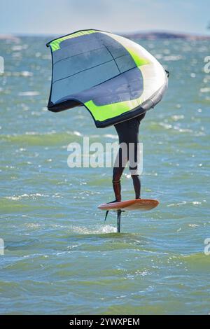 Der Mann ist Flügelfolierung mit handgehaltenem aufblasbarem Flügel und Tragflächensurfbrett im Meer im Sommer. Fahrer auf einem Windflügel-Board, surft in den Wellen. Stockfoto