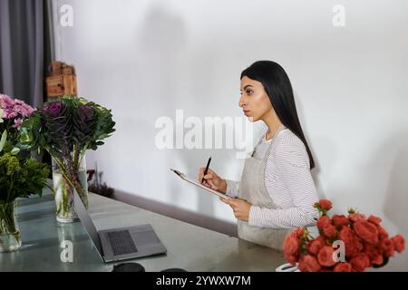 Eine brünette Floristin arrangiert in ihrem Blumenladen gekonnt leuchtende Blüten. Stockfoto