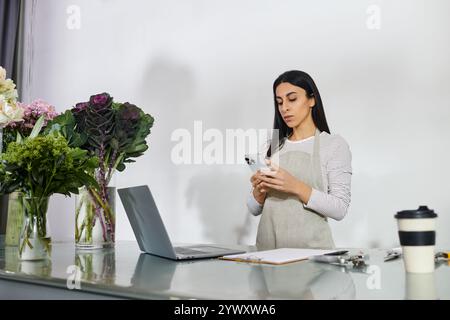 Eine engagierte Floristin erledigt tägliche Aufgaben in ihrem Blumenladen und überprüft ihr Handy auf Updates. Stockfoto