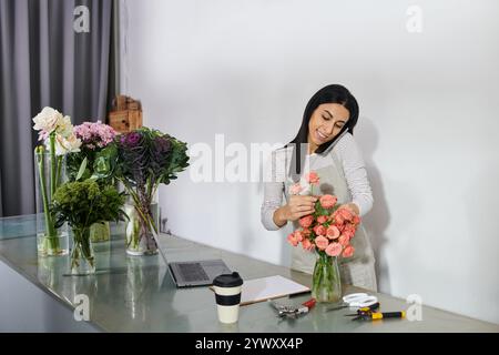 Eine gelernte Floristin arrangiert während eines Anrufs sorgfältig frische Blumen in ihrem Geschäft. Stockfoto