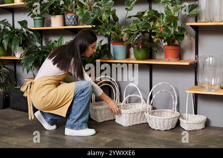 Die brünette Floristin arrangiert Körbe in ihrem charmanten Blumenladen, gefüllt mit Pflanzen. Stockfoto