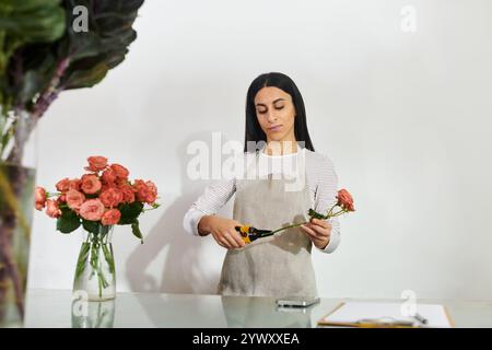 Die schöne brünette Floristin arrangiert geschickt Rosen, während sie ihr kleines Geschäft verwaltet. Stockfoto