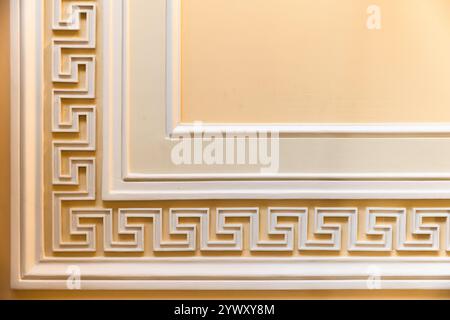 Mäander-Motiv vor gelbem Hintergrund. Klassische Wandverkleidung, Innendetails im Vintage-Stil, abstrakter architektonischer Hintergrund Stockfoto