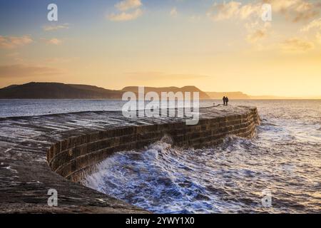 Ein Paar, das den Sonnenaufgang über dem Cobb im Lyme Regis in Dorset beobachtet. Stockfoto