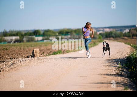 Schöne junge blonde Frau, die mit ihrem windhund auf dem Feld läuft. Stockfoto