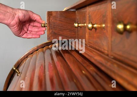 Nahaufnahme eines Mannes, der eine der Schubladen eines kunstvoll verzierten, massiven Holzschreibtisches aufreißt. Stockfoto