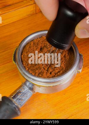 Die Finger greifen das Nadelverteilerwerkzeug eines Barista in einem Portafilterkorb und rühren das Bett mit gemahlenem Kaffee um, um ungleichmäßige Dichten zu entfernen. Stockfoto