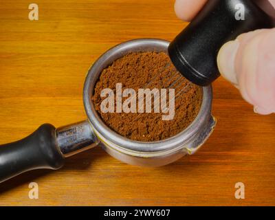 Die Finger greifen das Nadelverteilerwerkzeug eines Barista in einem Portafilterkorb und rühren das Bett mit gemahlenem Kaffee um, um ungleichmäßige Dichten zu entfernen. Stockfoto