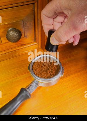 Eine Hand, die das Nadelverteilerwerkzeug eines Barista in einem Portafilterkorb hält und das Bett mit gemahlenem Kaffee umrührt, um ungleichmäßige Dichten zu entfernen. Stockfoto