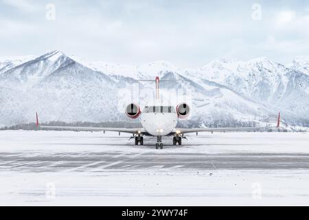 Vorderansicht eines regionalen Passagierflugzeugs, der am Winterflughafen vor dem Hintergrund hoher landschaftlicher Berge unterwegs ist Stockfoto