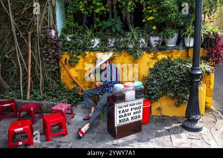Vietnam, Hoi an, 19.02.2024, Altstadt, Straßenladen, Verkäufer in Ruhe, roter kleiner Plastikhocker, vietnamesischer Strohhut, Straßenleben, Hitze, Sonne Stockfoto